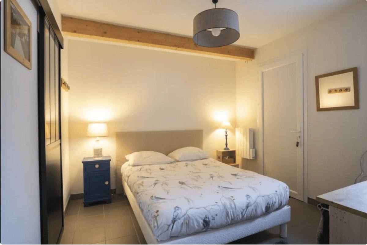 Le lit de 160 avec sa housse blanche à motifs, deux lampes de chevet allumées et une suspension grise