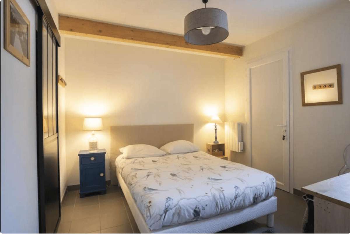 Le lit de 160 avec sa housse blanche à motifs, deux lampes de chevet allumées et une suspension grise