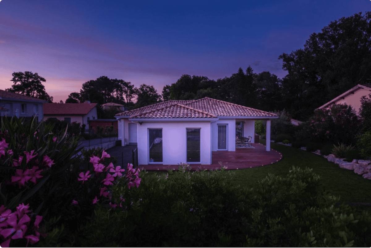 La maison au crépuscule, derrière des fleurs roses au premier plan