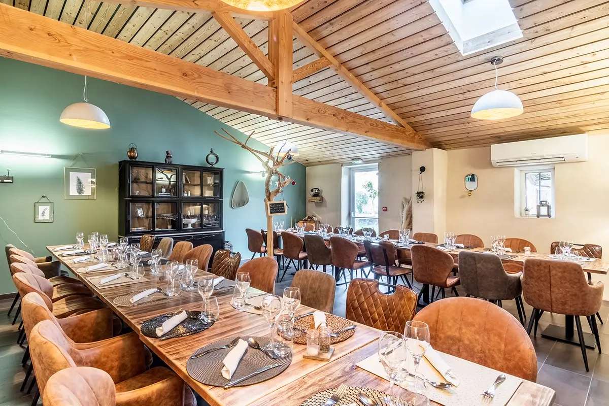Salle de restaurant aux tables dressées, sous une charpente en bois clair