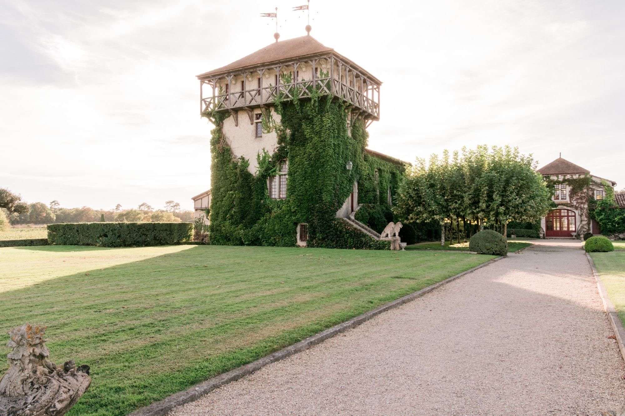 La tour du Château Smith Haut Lafitte couverte de vigne vierge, avec sa galerie en bois, au bout d'une allée de gravier bordée de pelouse