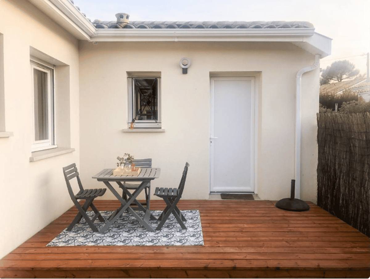 La terrasse en bois devant l'entrée du studio, avec une table, deux chaises pliantes et un tapis